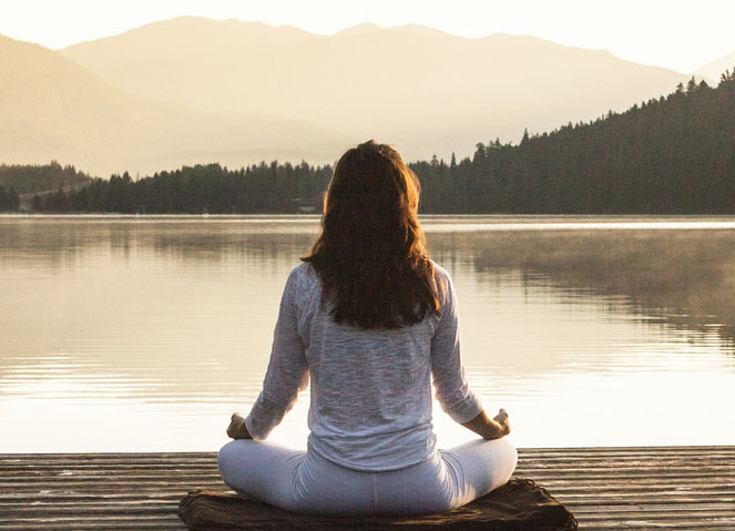 Woman meditating by lake.